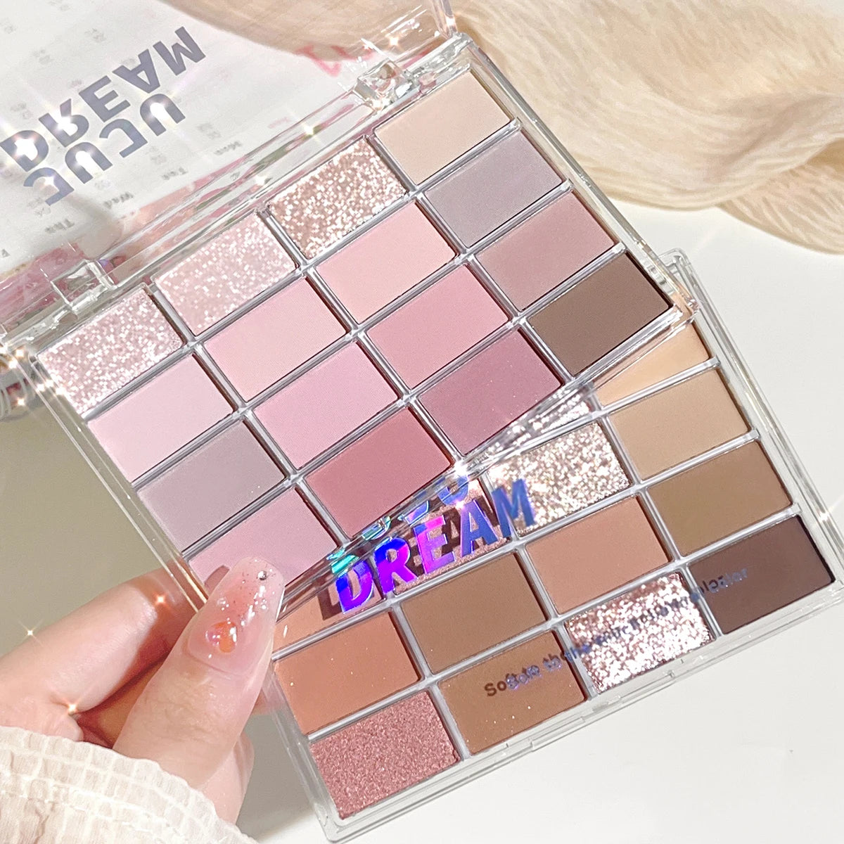 Palette de fards à paupières mates, dégradé rose, beige et pailleté, tenue à la main.