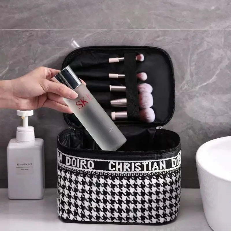 Trousse à maquillage pied-de-poule noir et blanc, ouverte, maquillage et brosses visibles.